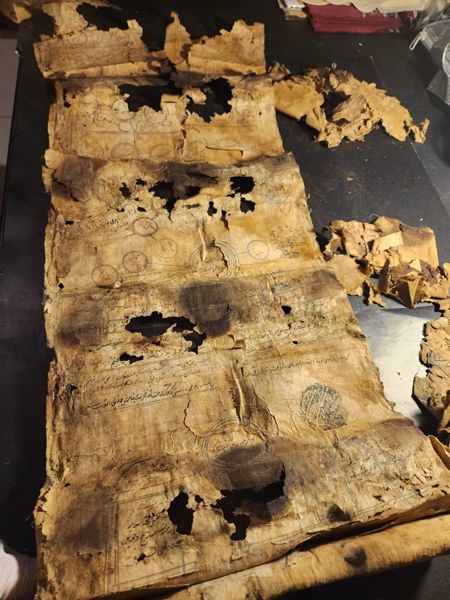 A scroll unrolled, showing severe burn and hole damage